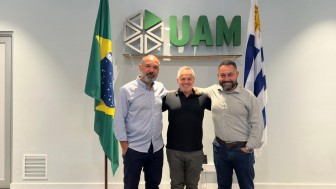 Imagem mostra tr&ecirc;s homens posando lado a lado em um ambiente interno institucional. Ao fundo, h&aacute; as bandeiras do Brasil e do Uruguai e o logotipo da UAM fixado na parede. Da esquerda para a direita est&atilde;o: o Presidente da CEASA/RS, Carlos Siegle, vestindo camisa social clara e cal&ccedil;a escura; o Presidente da UAM, Jos&eacute; Saavedra, ao centro, usando camisa polo preta e cal&ccedil;a escura; e o Diretor Operacional da CEASA/RS, Stefan Ludwig, vestindo camisa social clara e cal&ccedil;a jeans escura. Os tr&ecirc;s est&atilde;o sorrindo e com os bra&ccedil;os apoiados uns nos outros, demonstrando integra&ccedil;&atilde;o e coopera&ccedil;&atilde;o institucional.