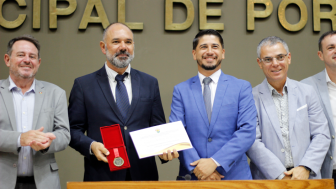 O presidente da CEASA/RS, Carlos Siegle, recebe a Comenda Porto do Sol no plen&aacute;rio da C&acirc;mara Municipal de Porto Alegre. Ao centro da imagem, ele segura a medalha da honraria e o certificado ao lado do vereador Giovane Byl, autor da homenagem, enquanto autoridades acompanham o momento durante a solenidade.